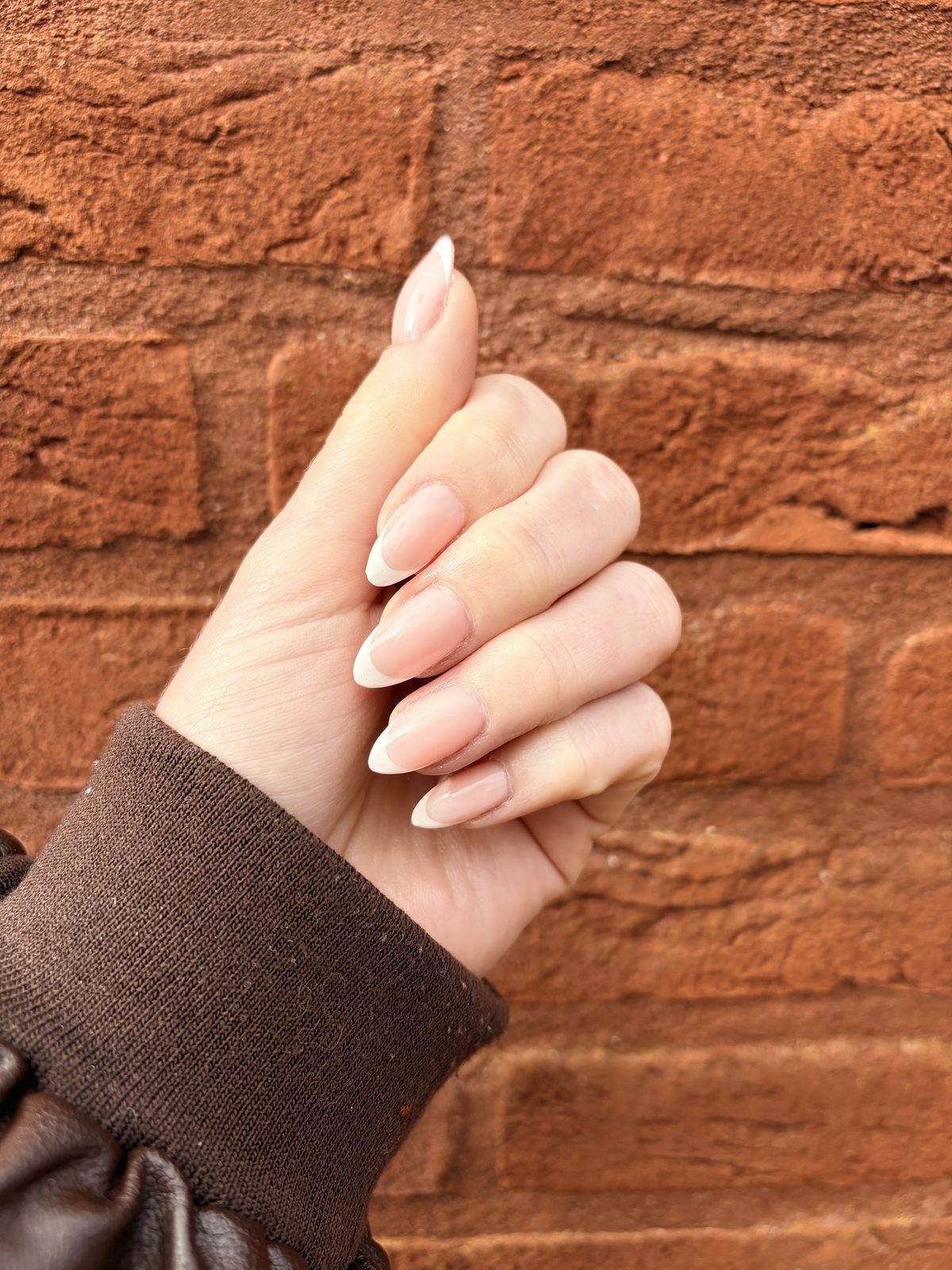 Naturelle amandelnagels tegen een bakstenen muur