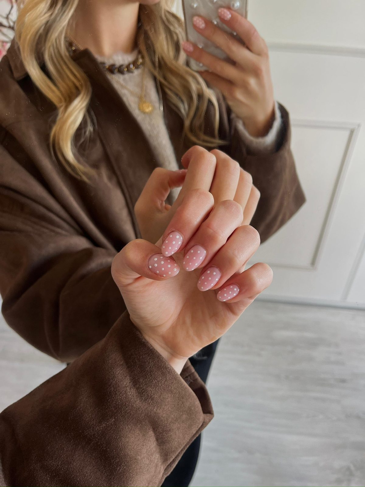 Roze nagels met witte stipjes, hand voor een bruine blazer