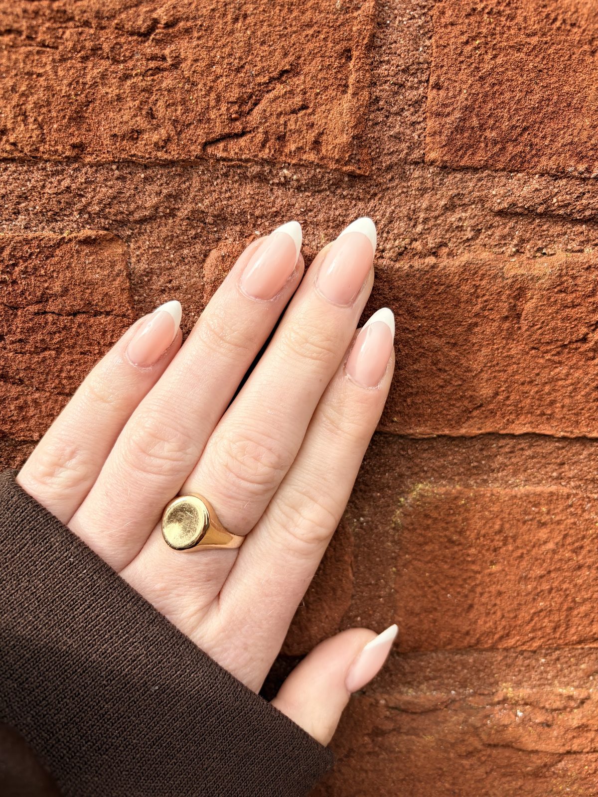 Lange amandelnagels met witte tip tegen een bakstenen muur